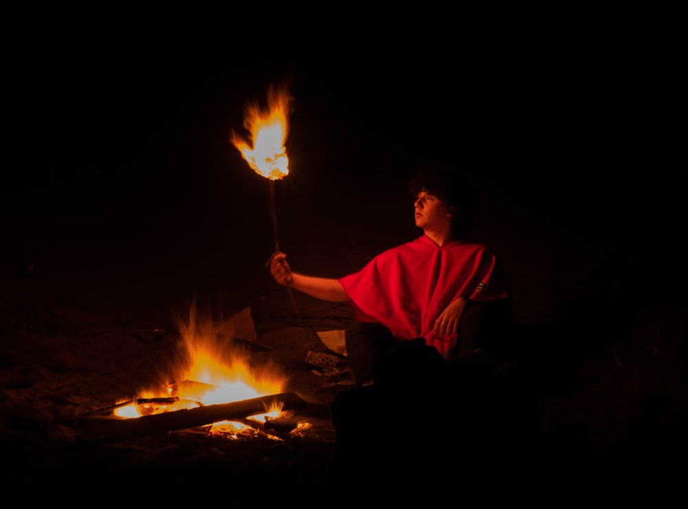 a man holding a stick by a fire at night