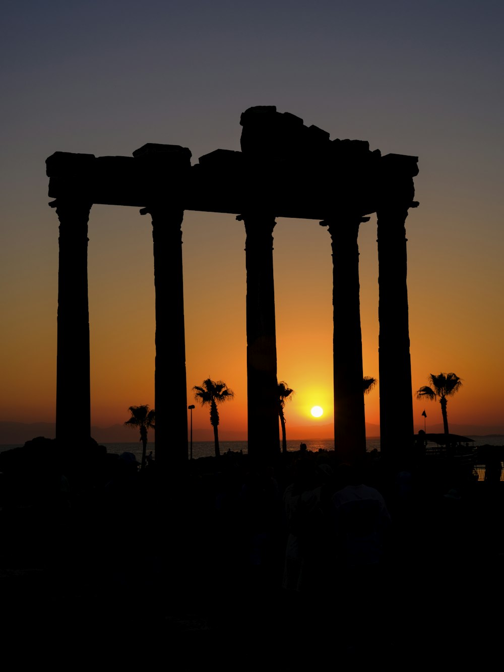 a silhouette of a structure with palm trees and a sunset in the background