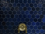 A wall covered with dark blue hexagonal tiles, featuring a central antique brass faucet with intricate handles.