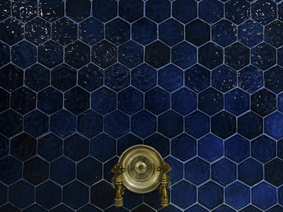 A wall covered with dark blue hexagonal tiles, featuring a central antique brass faucet with intricate handles.