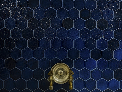 A wall covered with dark blue hexagonal tiles, featuring a central antique brass faucet with intricate handles.