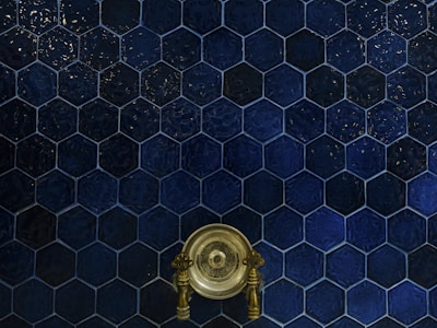 A wall covered with dark blue hexagonal tiles, featuring a central antique brass faucet with intricate handles.