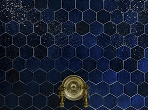 A wall covered with dark blue hexagonal tiles, featuring a central antique brass faucet with intricate handles.