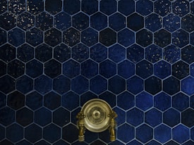 A wall covered with dark blue hexagonal tiles, featuring a central antique brass faucet with intricate handles.