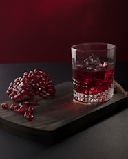 a glass of red liquid next to a glass with berries