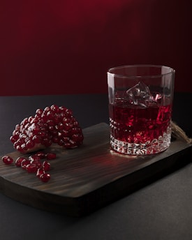 a glass of red liquid next to a glass with berries