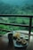 A serene view of lush green hills and rice paddies seen from a balcony, with a wooden table in the foreground featuring a mug, a plate of pancakes, a bowl of sauce, and a dish of fries.
