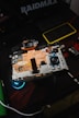 An open electronic device with visible internal components, including circuitry and connectors. The device rests on a dark surface with a logo and another small gadget visible nearby, indicating a focus on technology and repair.