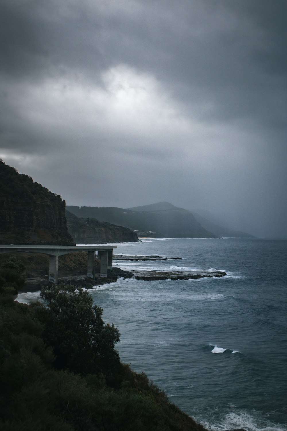 a body of water with a bridge and hills in the background