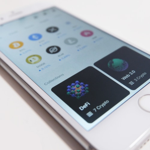 A smartphone displays a cryptocurrency app interface with logos of different cryptocurrencies like Bitcoin, Dogecoin, and Stellar. The app includes sections for various collections like DeFi and Web 3.0, with the number of cryptos listed under each.