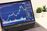 A sleek multi-monitor trading setup glowing with green and red candlestick charts against a dark grey background.