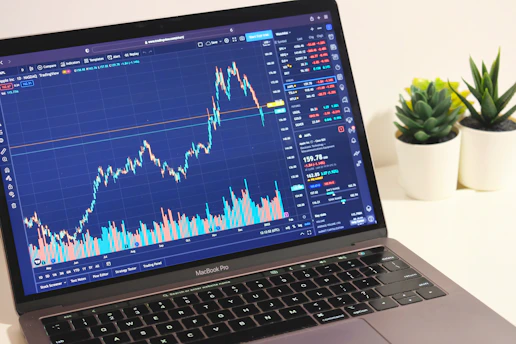 A close-up of a trader's hands analyzing colorful stock charts on multiple screens in a cozy home office.