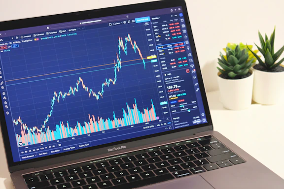A close-up of a laptop screen displaying a trading chart with colorful candlesticks and indicators, set on a wooden desk with a cup of coffee nearby.