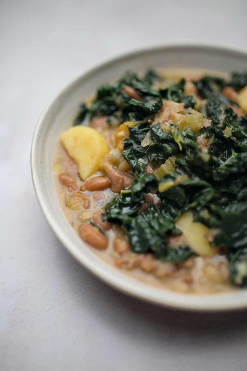 A bowl of white bean, potato and dark leafy green stew, close to a caldo galego
