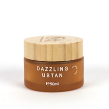 A small, round cosmetic jar with a wooden lid and frosted brown glass container. The product name 'Dazzling Ubtan' is printed in white uppercase letters on the front, along with the volume '50ml'.