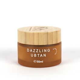 A small, round cosmetic jar with a wooden lid and frosted brown glass container. The product name 'Dazzling Ubtan' is printed in white uppercase letters on the front, along with the volume '50ml'.