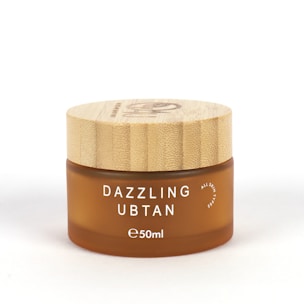 A small, round cosmetic jar with a wooden lid and frosted brown glass container. The product name 'Dazzling Ubtan' is printed in white uppercase letters on the front, along with the volume '50ml'.