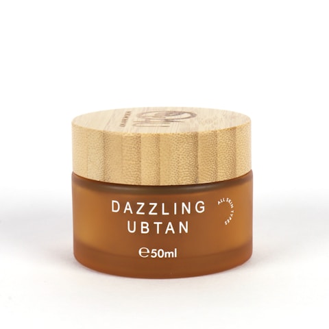 A small, round cosmetic jar with a wooden lid and frosted brown glass container. The product name 'Dazzling Ubtan' is printed in white uppercase letters on the front, along with the volume '50ml'.