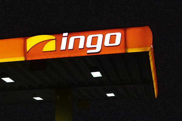 A brightly illuminated gas station canopy at night with the logo 'ingo' displayed prominently in white and a partially yellow background on an orange panel.
