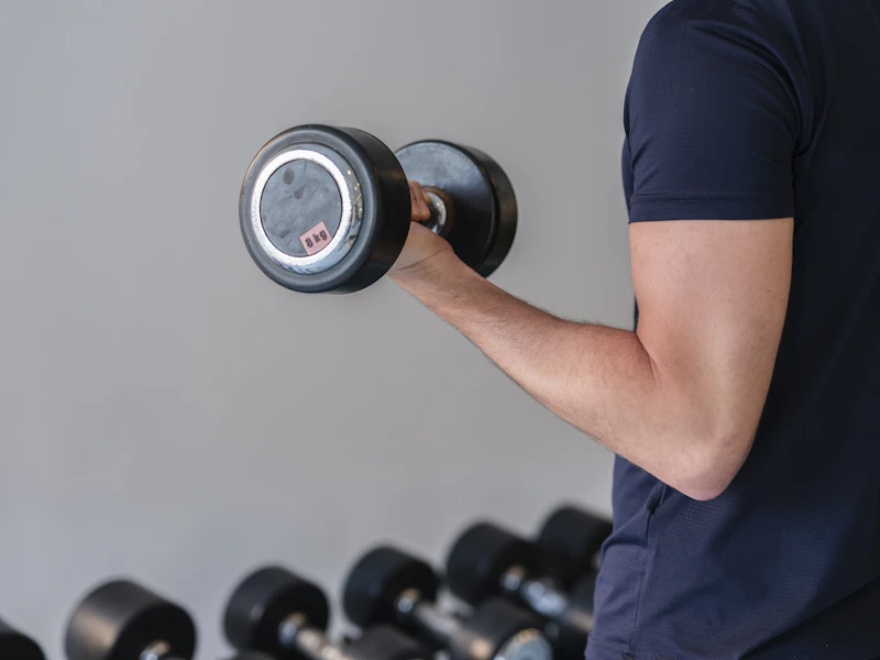 Close-up of an athlete curling a dumbbell beside a gym weight rack