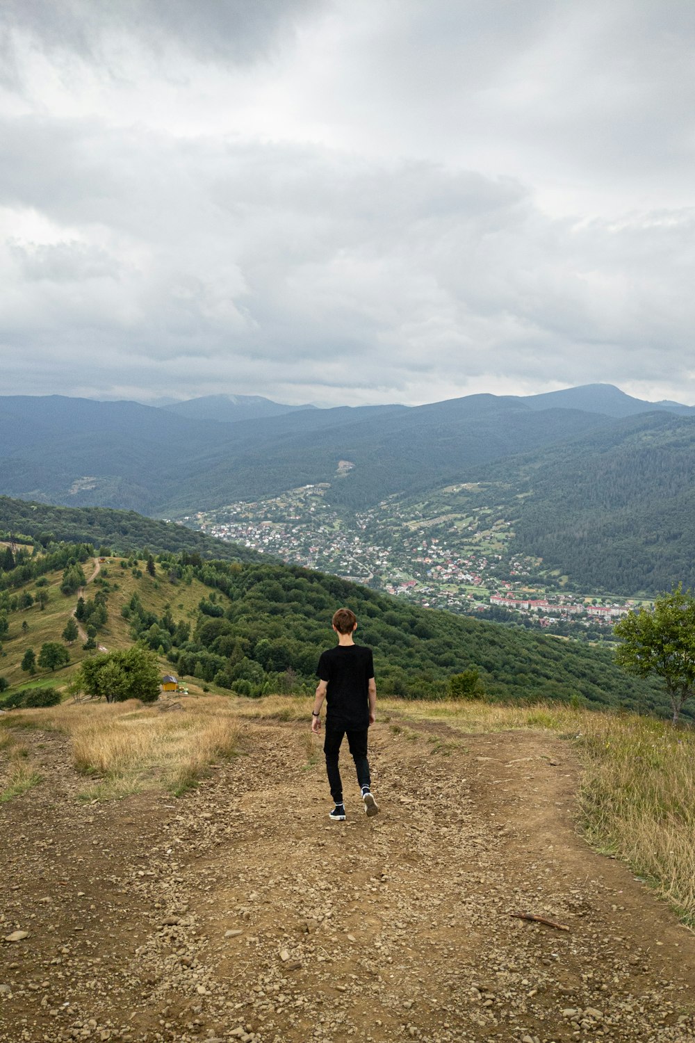 a man standing on a dirt road with hills and trees in the background