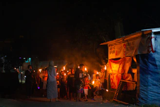 A group of diverse community members gathered around a glowing torch symbolizing hope and unity during an outdoor evening event.