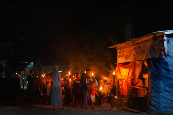 A group of diverse community members gathered around a glowing torch symbolizing hope and unity during an outdoor evening event.