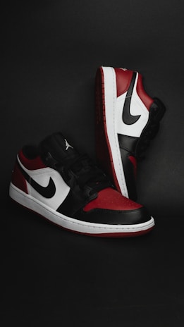 A pair of stylish athletic shoes in black, white, and red colors with distinctive branding. The shoes are positioned against a dark background, showcasing their sleek design and detailed craftsmanship.