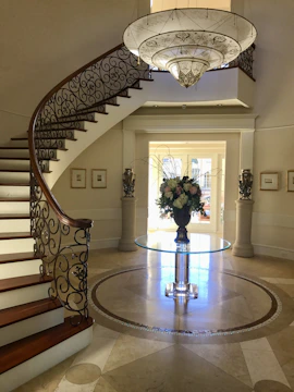 A grand entryway showcasing soft gray marble floors and a statement gold chandelier.