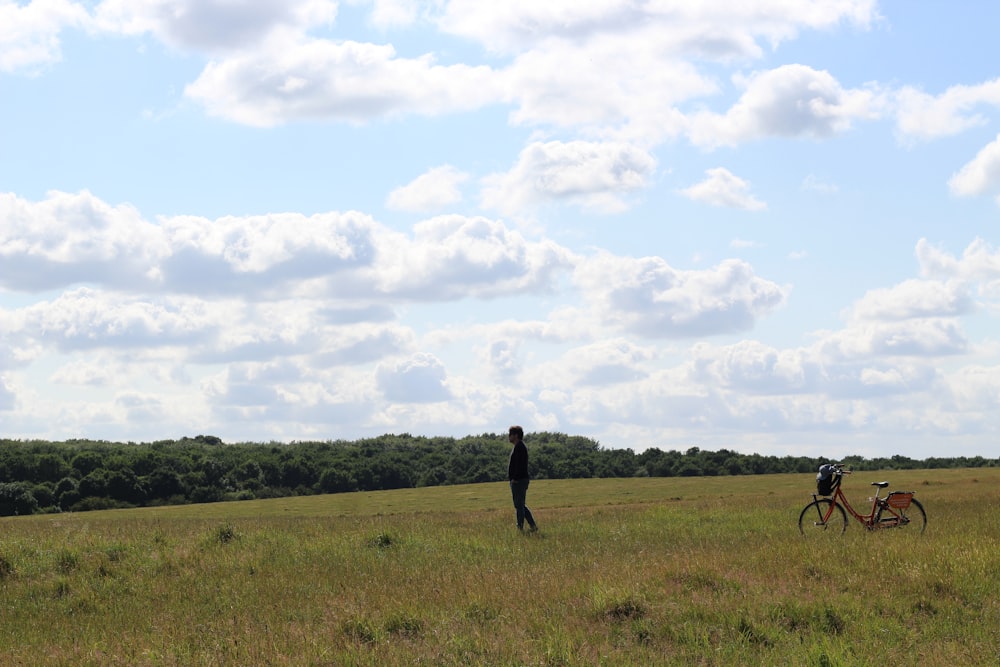 a person standing in a field with a bicycle and a person in the distance