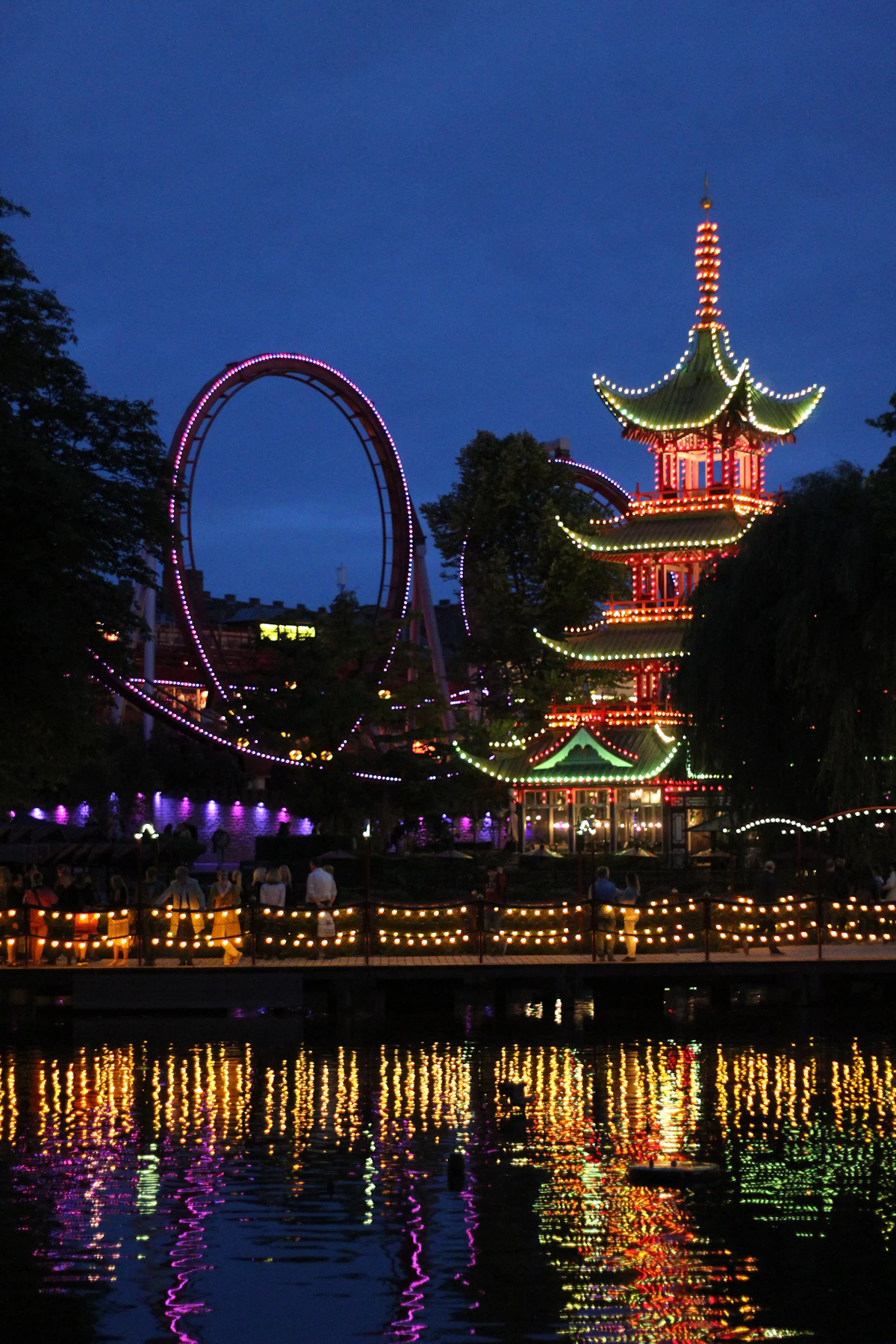 Tivoli Gardens in Copenhagen lit up at night with a pagoda and rides