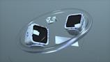 Two cube-shaped objects with black screens and white surfaces decorated with blue geometric patterns float within a large metallic ring. A compact keyboard and two game controllers accompany the cubes, all set against a minimalistic gray background.
