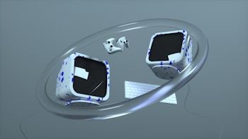 Two cube-shaped objects with black screens and white surfaces decorated with blue geometric patterns float within a large metallic ring. A compact keyboard and two game controllers accompany the cubes, all set against a minimalistic gray background.