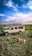 Several safari vehicles are parked on a grassland, with a lion lying in the foreground. The sky is mostly clear with some wispy clouds. A few people are observed on top of one of the vehicles.