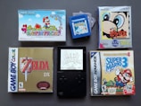 A collection of vintage video game cartridges and cases for different Nintendo systems, including Game Boy, Game Boy Color, and Game Boy Advance. Visible games are 'Super Mario Advance', 'The Legend of Zelda: Link's Awakening DX', 'Kirby's Dream Land', 'Super Mario Advance 4: Super Mario Bros. 3', and a 'Pokemon' cartridge. The layout suggests a nostalgic gaming theme.