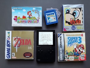 A collection of vintage video game cartridges and cases for different Nintendo systems, including Game Boy, Game Boy Color, and Game Boy Advance. Visible games are 'Super Mario Advance', 'The Legend of Zelda: Link's Awakening DX', 'Kirby's Dream Land', 'Super Mario Advance 4: Super Mario Bros. 3', and a 'Pokemon' cartridge. The layout suggests a nostalgic gaming theme.