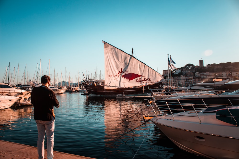 a person standing next to a sailboat in a harbor