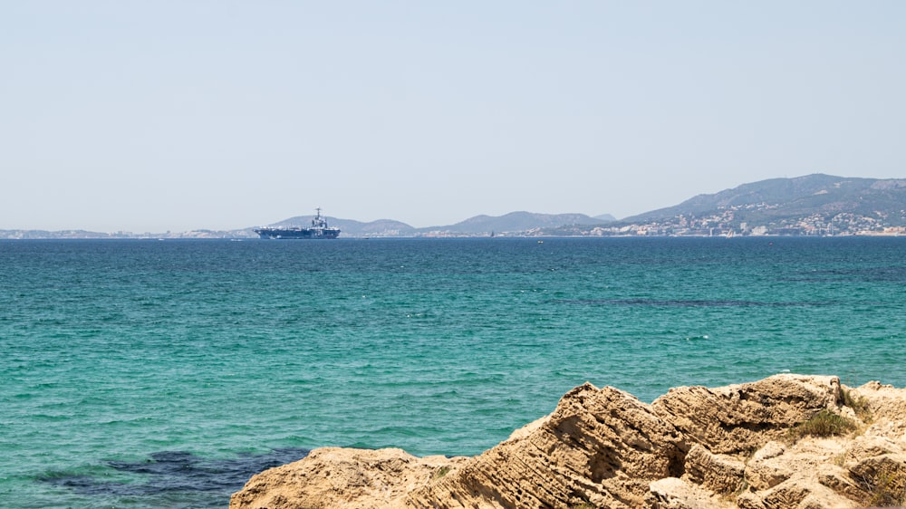 a rocky beach with a large ship in the distance