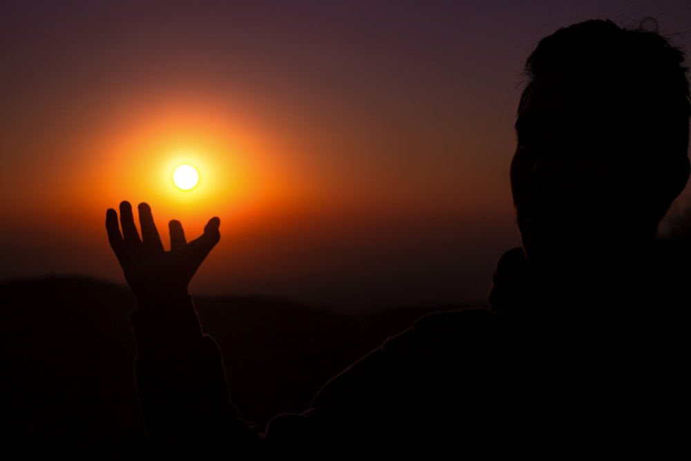 a person holding their hands up in front of a sunset