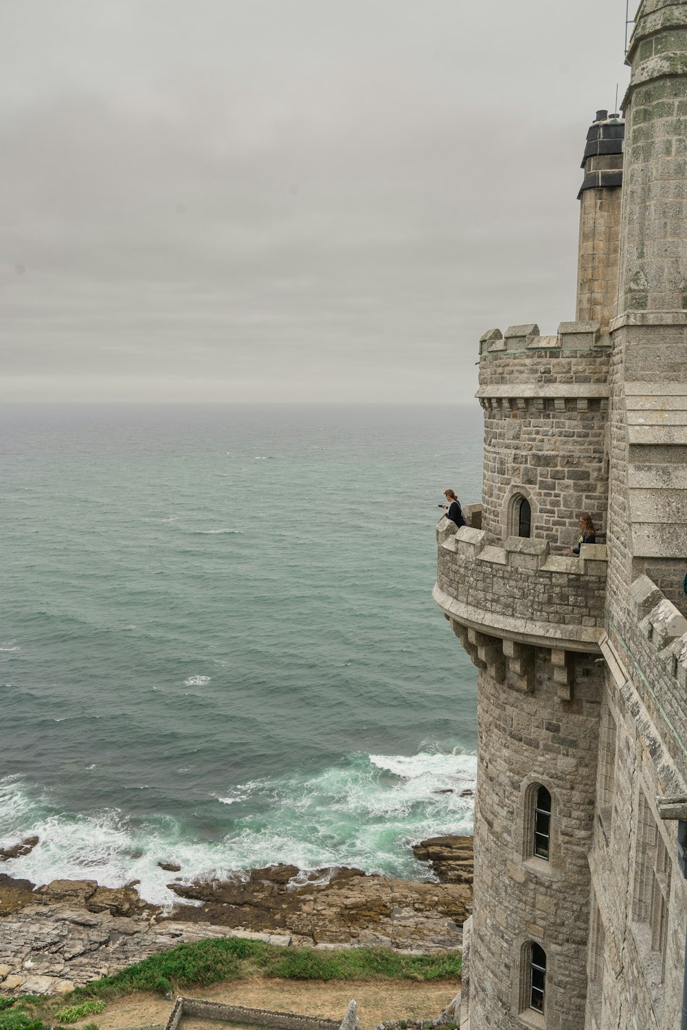 a stone building with a person standing on top of it by the water