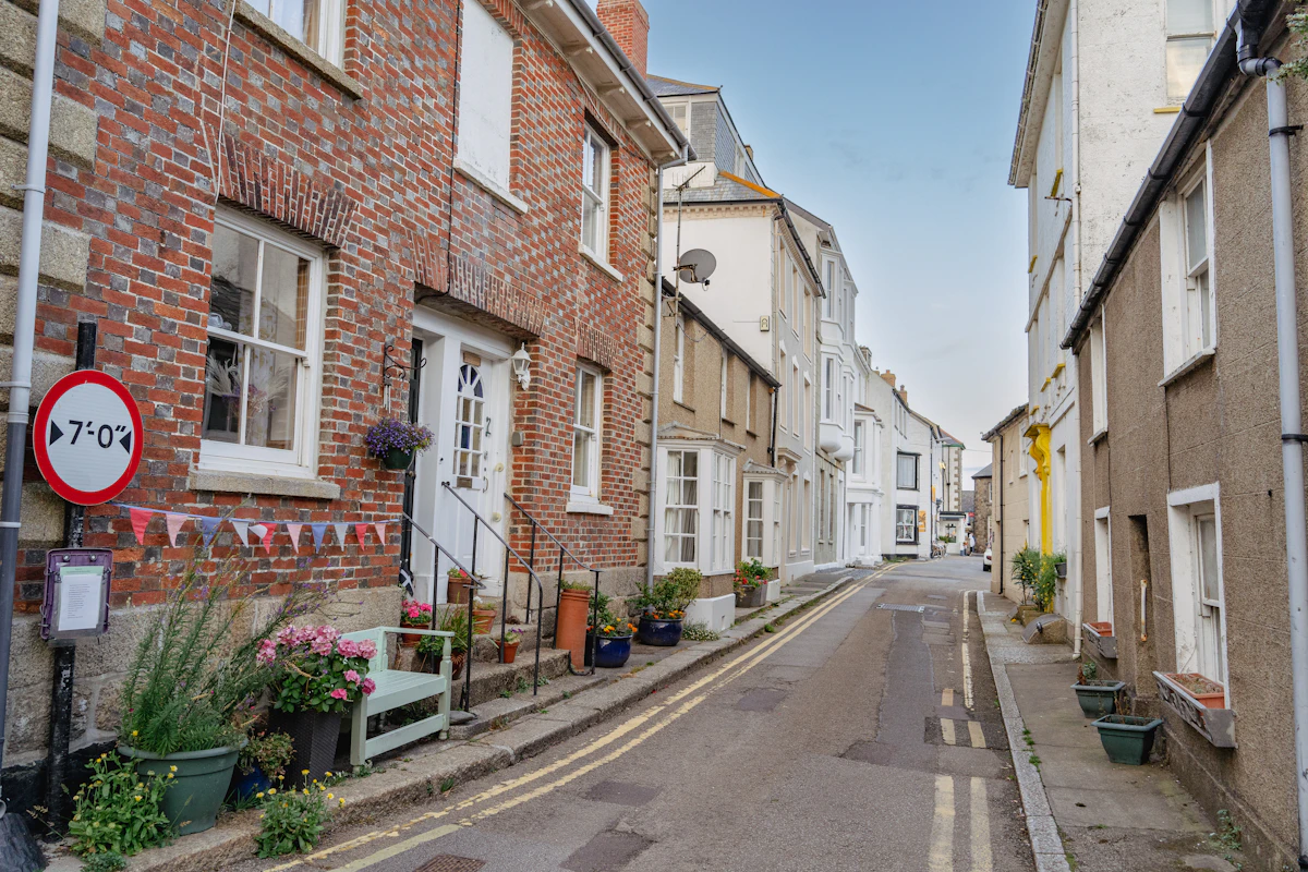 A narrow street of brick terraced houses with front doors opening onto the pavement