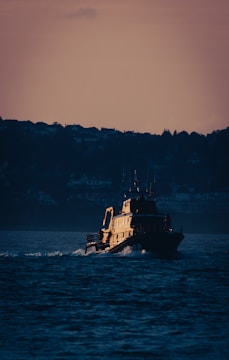 Offshore support vessel navigating calm sea near oil platform at sunset.