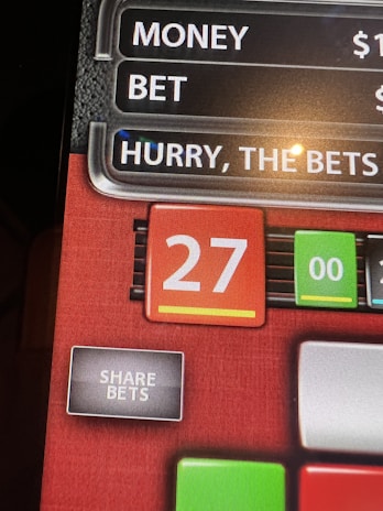 A digital display screen showing a casino betting interface, with text prompting to hurry bets and a highlighted number 27 in red. There are options for betting amounts and a 'share bets' button.