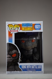 A boxed Funko Pop! vinyl figure of Kong holding a battle axe, from the movie Godzilla vs. Kong. The packaging displays vibrant colors and features a large image of the character with red eyes. The figure itself is visible through clear plastic within the box.