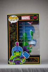 A Funko Pop! collectible figure encased in a box with vibrant illustrations and branding. The character depicted is green with a blue helmet and armor, wielding a large hammer. The box features the Marvel logo and the number 907.