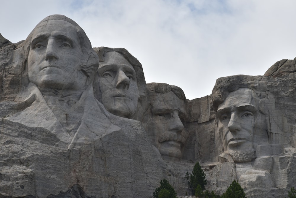 un groupe de visages sculptés dans un rocher avec le Mémorial national du Mont Rushmore en arrière-plan