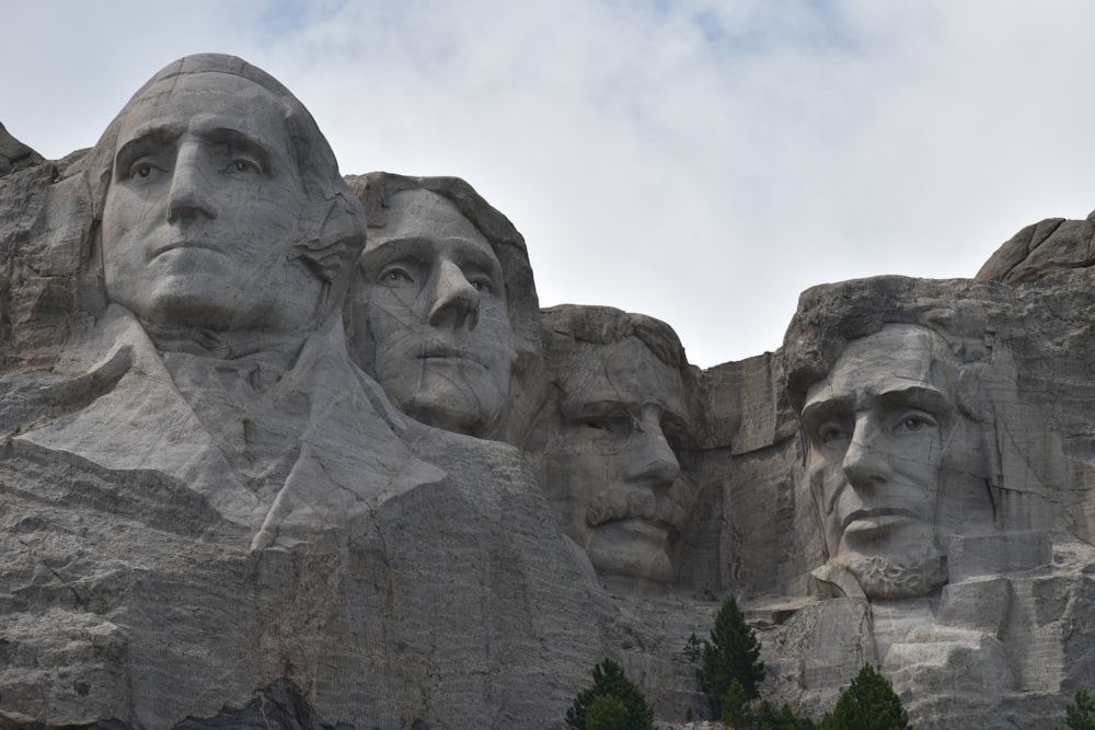 a group of faces carved into a rock with Mount Rushmore National Memorial in the background