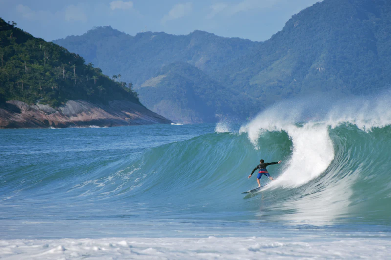 Surfista em onda com morros verdes ao fundo