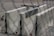 Several large concrete barriers are placed closely together on a paved surface. There are some metal brackets attached to the barriers, and the scene is viewed through a chain-link fence, which creates a blurred effect in the foreground.