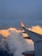 An airplane wing with a red AirAsia logo extends over a vast expanse of fluffy white clouds. The clouds are illuminated with a warm golden hue by the sunlight, contrasting with the clear blue sky above.